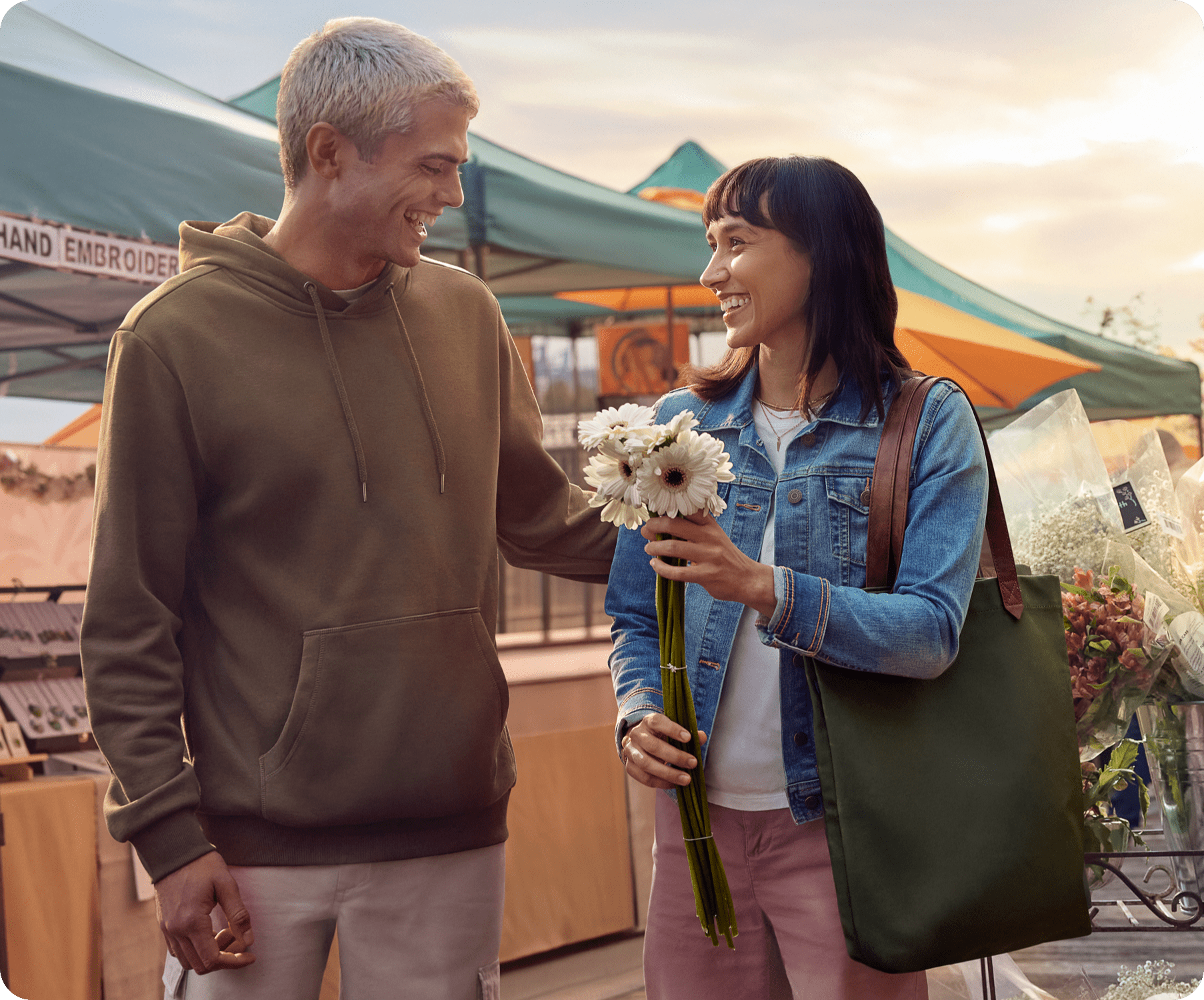 A couple is walking through a market while the woman is holding a flower