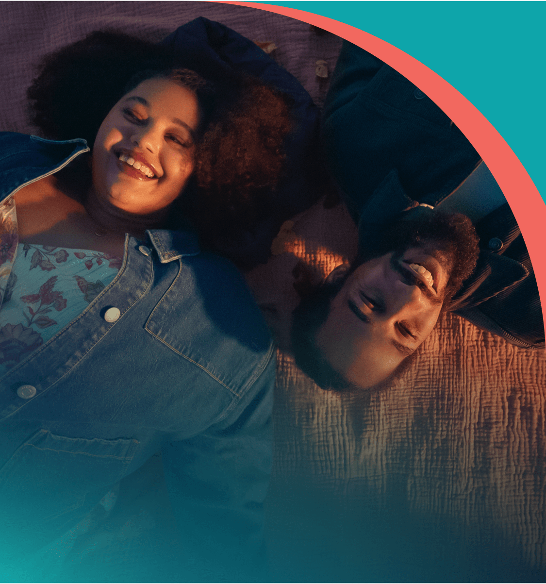 A couple laying down smiling on a blanket.