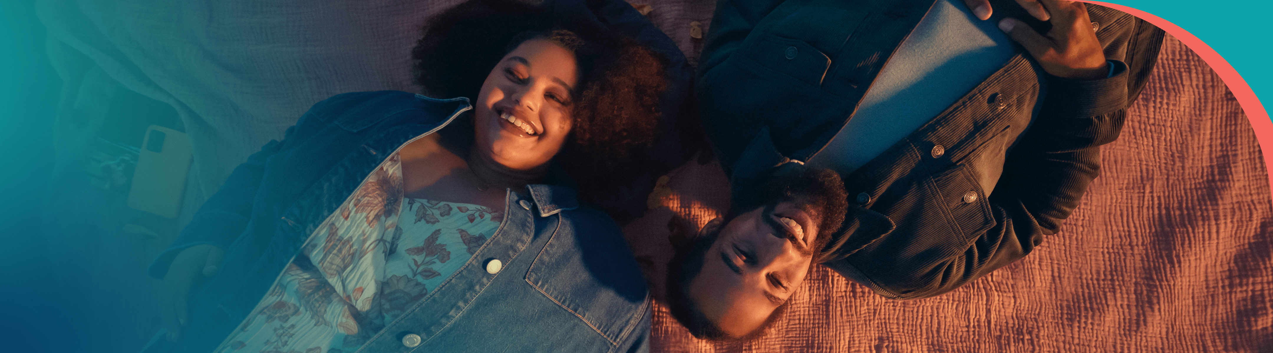 A couple laying down smiling on a blanket.